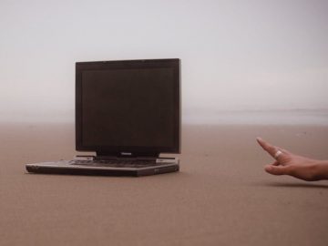 Un homme essaie d'attraper un Laptop, les deux sur le sable d'une plage.